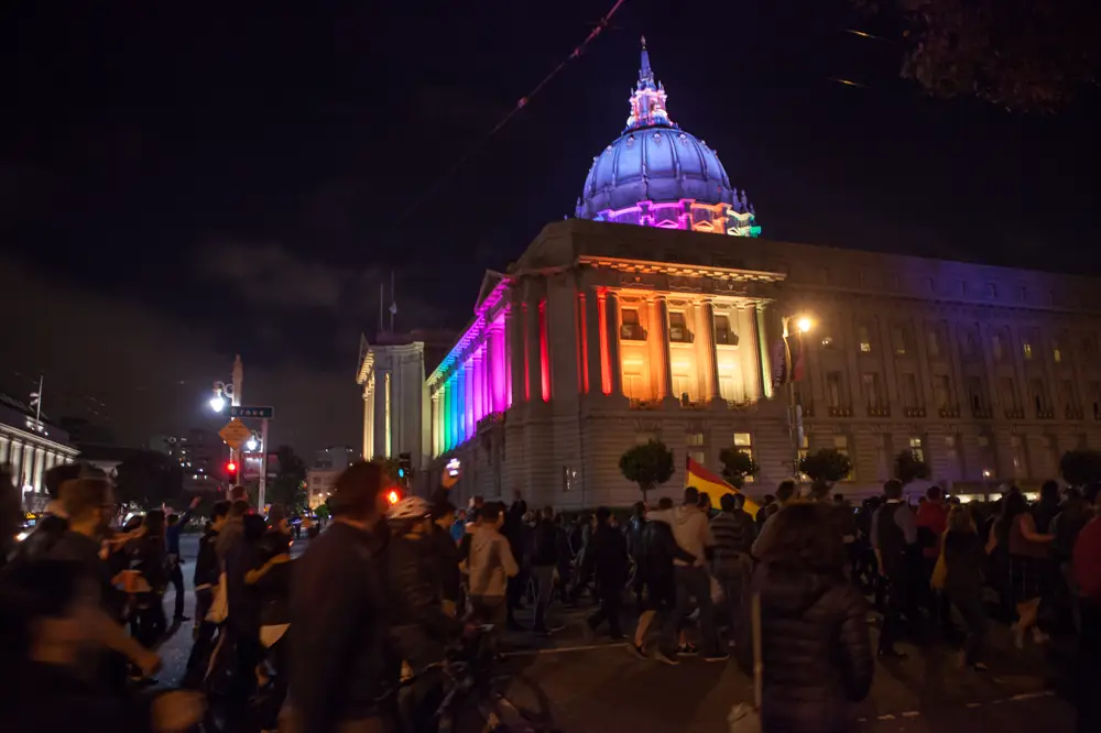 Marchers pass San Francisco City Hall lit in rainbow Pride colors during a vigil for the Orlando victims